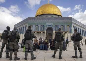 Israeli policemen stand guard in front of Muslim women praying in front of the Dome of the Rock mosque as a group of religious Jewish men and women visit the Temple Mount, which is known to Muslims as the Haram al-Sharif (The Noble Sanctuary), at the Al-Aqasa mosques compound in the old city of Jerusalem on April 20, 2022. Hundreds of Jewish pilgrims escorted by Israeli police visit the site during the Pesach holiday as Jews are allowed to visit at certain times, but they are prohibited from praying there. Incidents at the Al-Aqsa mosque compound, the holiest site in Judaism and the third-holiest in Islam, have triggered repeated rounds of violence over the past century. (Photo by MENAHEM KAHANA / AFP)
