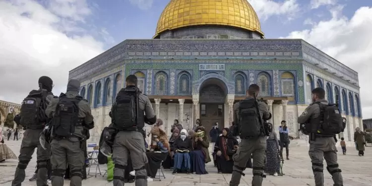 Israeli policemen stand guard in front of Muslim women praying in front of the Dome of the Rock mosque as a group of religious Jewish men and women visit the Temple Mount, which is known to Muslims as the Haram al-Sharif (The Noble Sanctuary), at the Al-Aqasa mosques compound in the old city of Jerusalem on April 20, 2022. Hundreds of Jewish pilgrims escorted by Israeli police visit the site during the Pesach holiday as Jews are allowed to visit at certain times, but they are prohibited from praying there. Incidents at the Al-Aqsa mosque compound, the holiest site in Judaism and the third-holiest in Islam, have triggered repeated rounds of violence over the past century. (Photo by MENAHEM KAHANA / AFP)