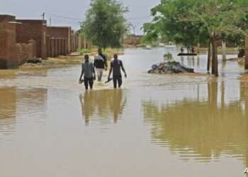 People wade through flood water in Managil city in al-Gezira state, around 250Km south of the capital, on August 23, 2022. - Sudan declared a state of emergency due to floods in six states, including River Nile. Since the start of the devastating rainy season, thousands of Sudanese families have been left homeless, sheltering under tattered sacking. (Photo by Ebrahim Hamid / AFP)